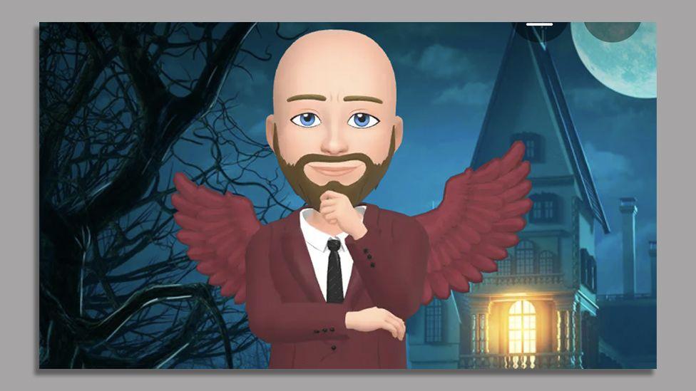 An emoji character, "Dom" which Lipscombe used on Snapchat. He is bald and he has a goatee and moustache. He is wearing a maroon suit and tie and has maroon-coloured wings. He stands in front of an old house with a light on inside and to the left there is a tree with no leaves. It is night time in the cartoon scene.