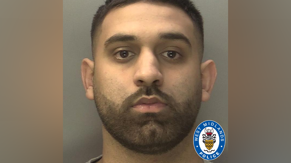 A police mugshot of a man with short dark hair and a short dark beard. He is looking directly at the camera with a plain background behind him.