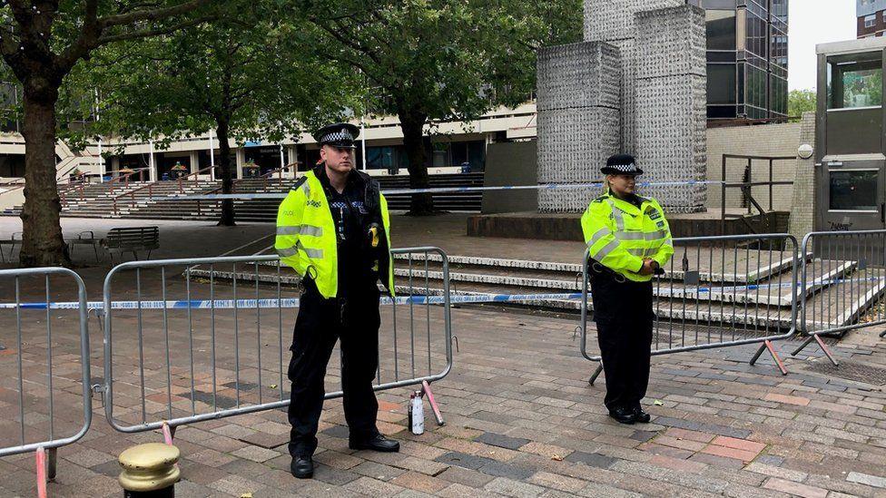 A male and a female police officer stand guard at a police cordon in Portsmouth's pedestrianised Guildhall Square. In the background are steps leading to the city council's headquarters.