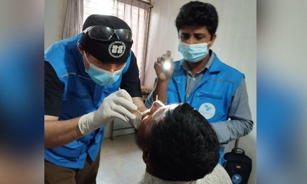 Mr Lugo (L) working on a patient with another dentist stood next to him shining a light.