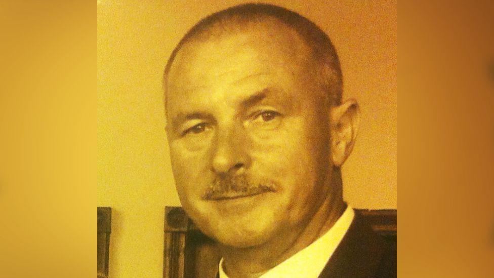 A head and shoulders image of Harry Roy Veevers that is seen with an orange filter. The collar of a white shirt and dark jacket can be seen.