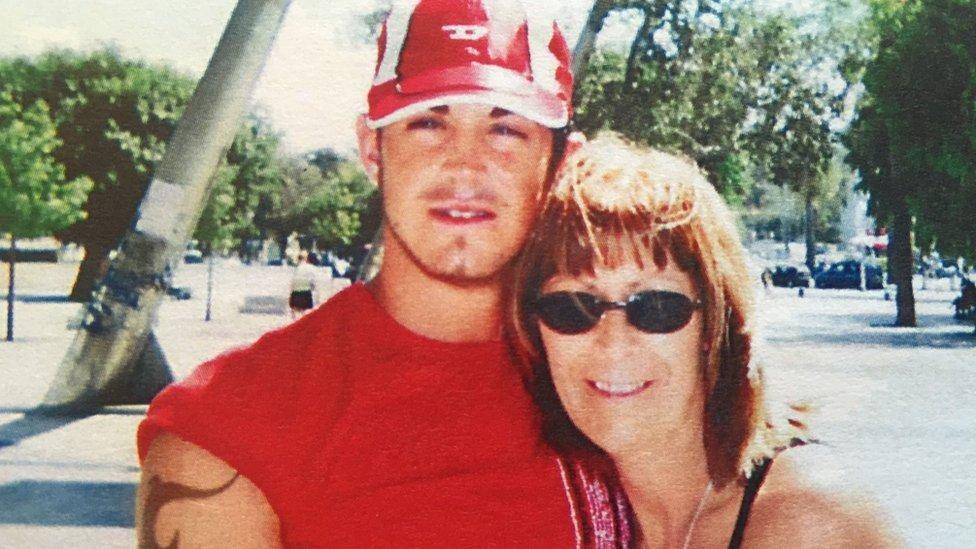 An archive picture of Michael Porter with his mother Jean Halon. He is wearing a red baseball cap and a red sleeveless tshirt. She has shoulder-length brown hair and is wearing sunglasses.