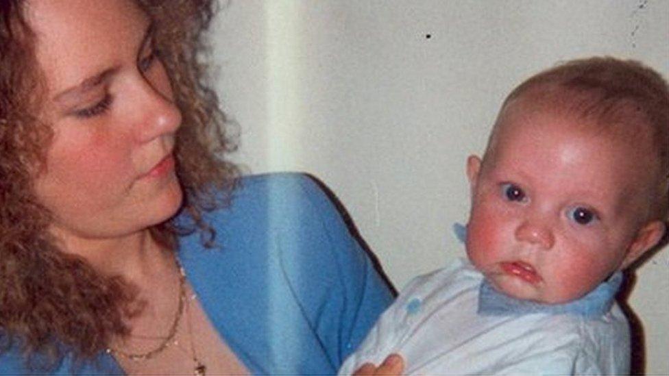 Nicola Payne dressed in a blue jacket with a gold neckless holding a baby wearing white