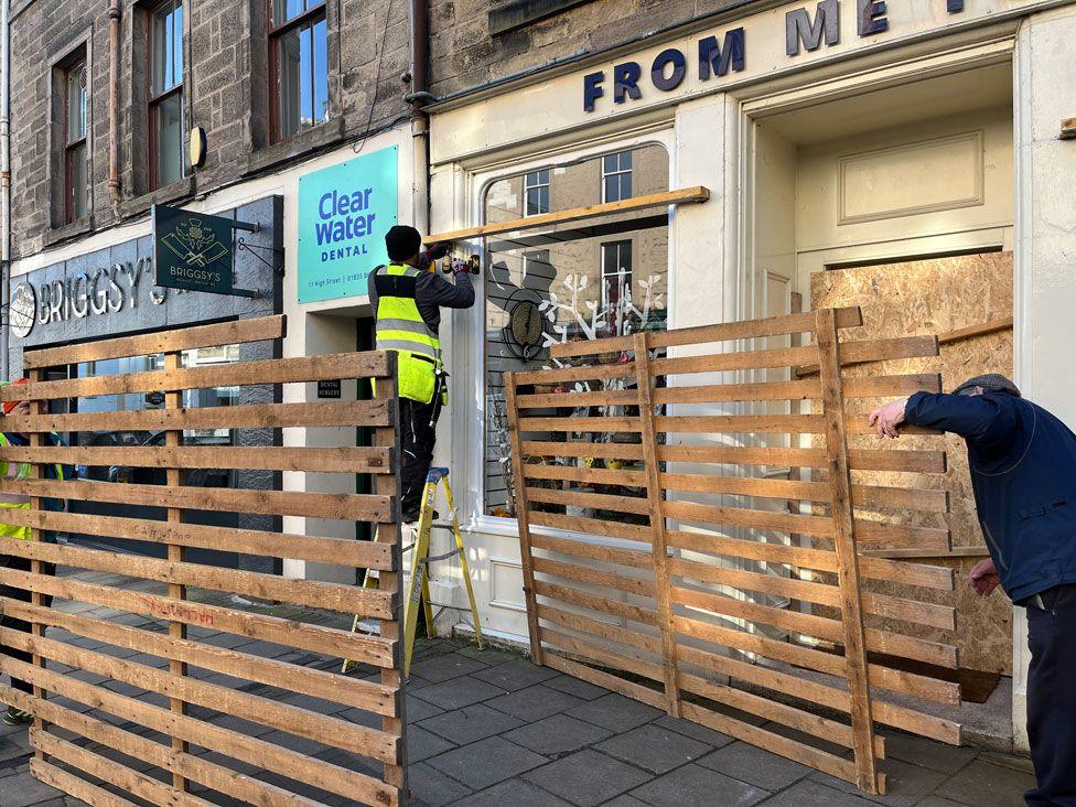 Two people working to put up boards on a shop front in Jedburgh ahead of its historic ba' game