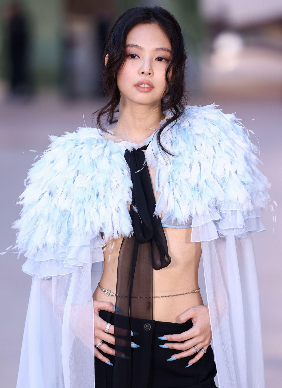 Jennie Kim posing in a white shawl with exposed torso and black trousers