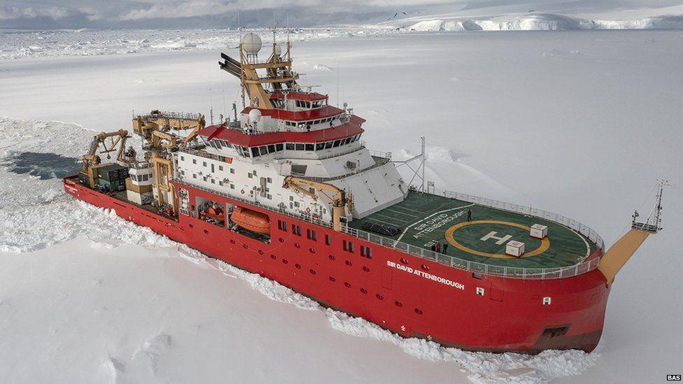 The RSS Sir David Attenborough is a large red ship with a green helipad on the front. It is shown sailing through icy, snow-covered water