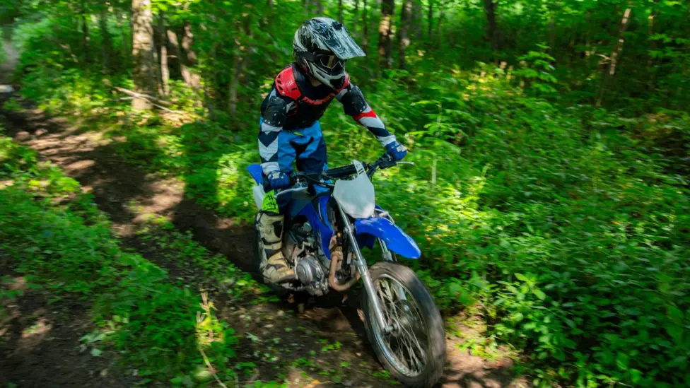 A biker in a helmet rides a blue off-road motorbike through a woodland