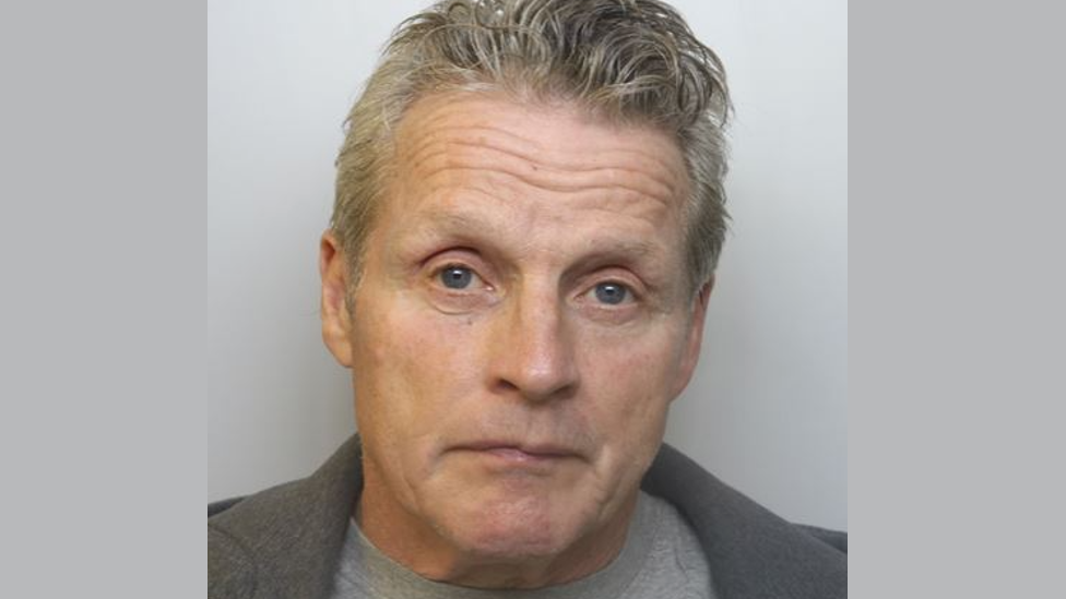 Ian Barnes has grey hair and is wearing a light grey t-shirt underneath a darker grey jacket