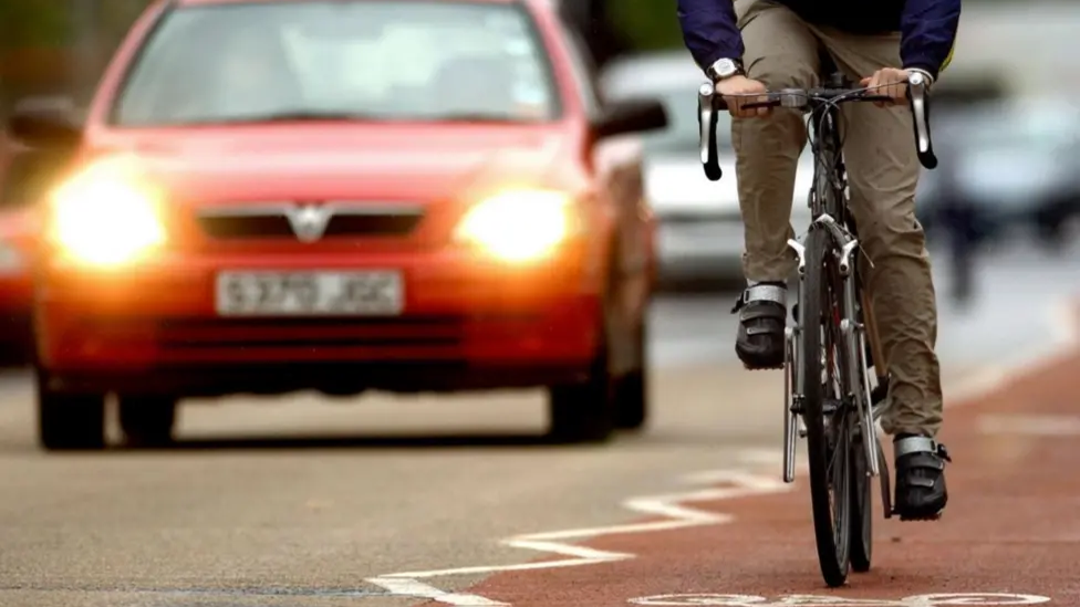 An anonymous cyclist is in a cycle lane on a main city road, as cars pass him on his right