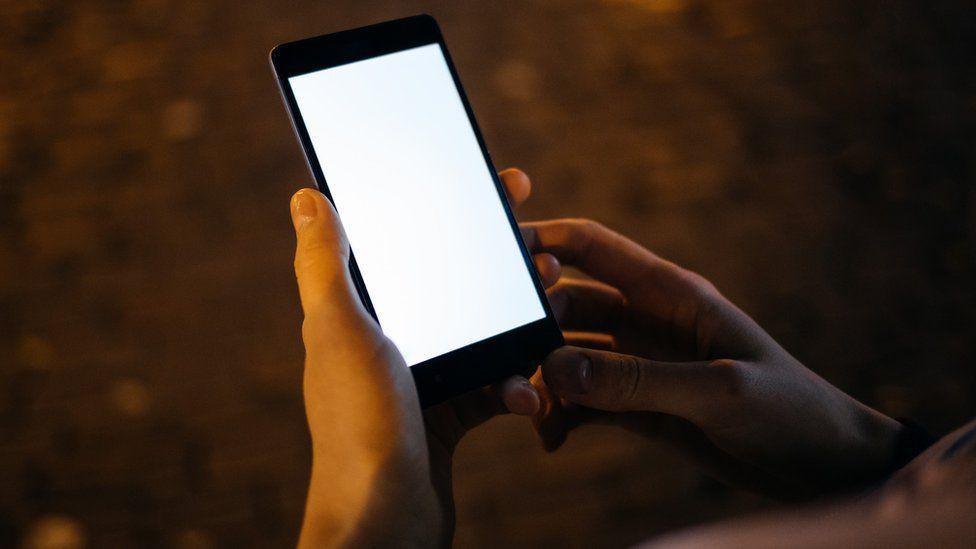 A hand holding a phone with a white screen