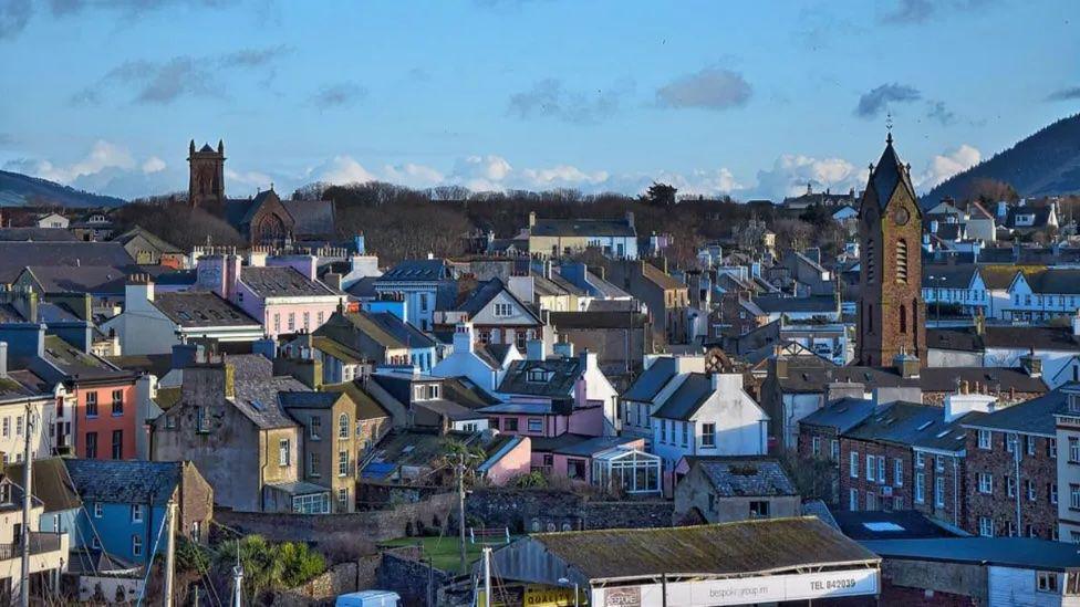 A high up view of rooftops with two church towers and a hill in the background with a clear blue sky.