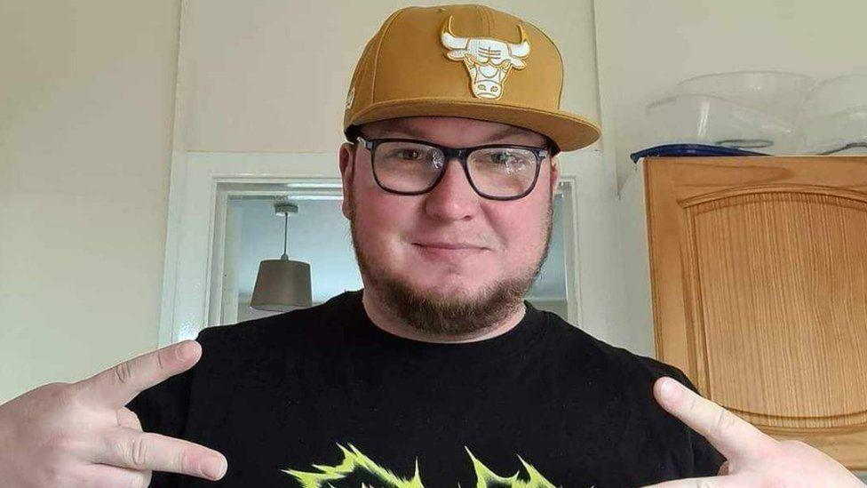 Michal Kaminski, a man with a beard wearing a yellow cap, a black t-shirt and glasses