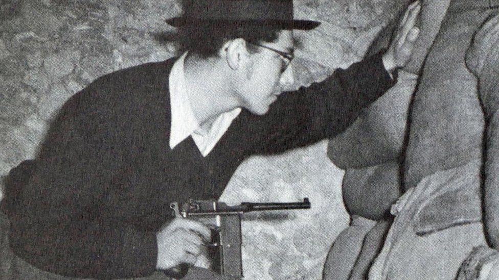 A Haganah (Jewish Underground) fighter is pictured just before the start of the Israeli war of independence in 1948. He is wearing a hat and glasses and is pointing a gun.