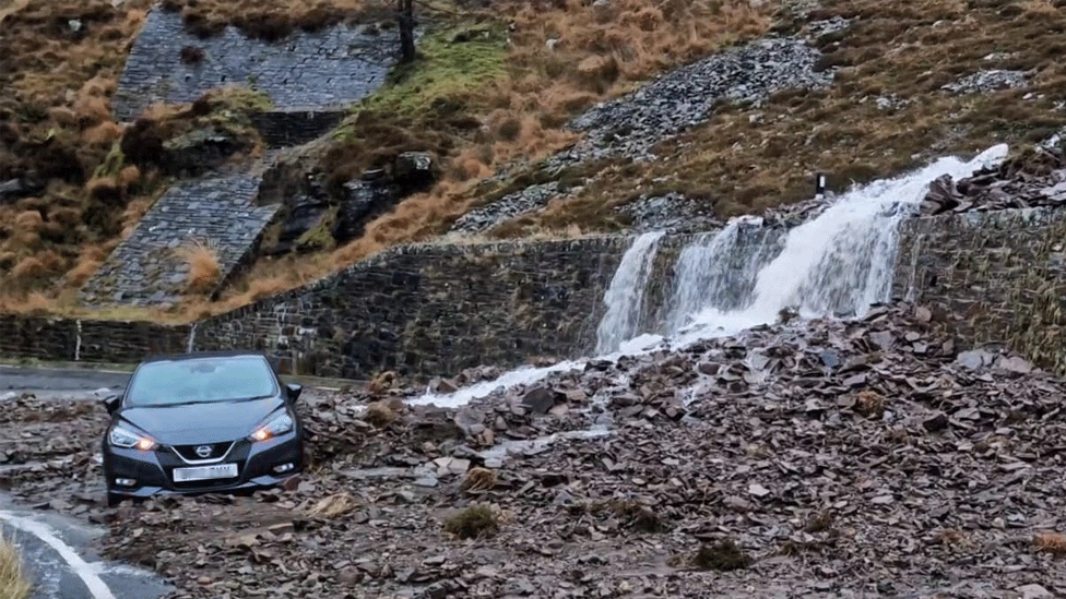 A car appears to have been side swiped by the landslip, leaving it partly surrounded by debris