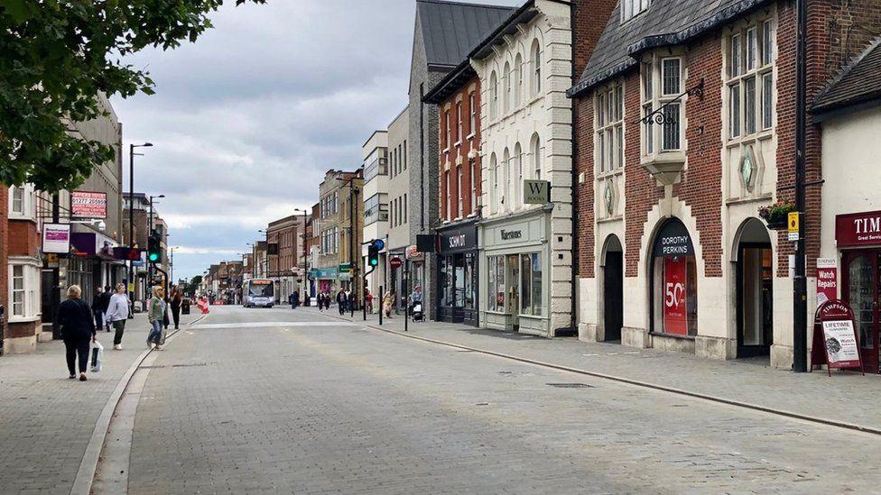 A general view of Brentwood High Street with its various shops, restaurants and people milling about on a cloudy day.