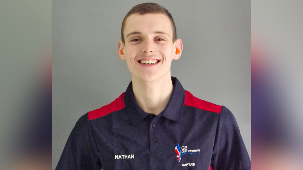 A teenage boy, wearing a GB deaf swimming polo shirt, smiles at the camera.