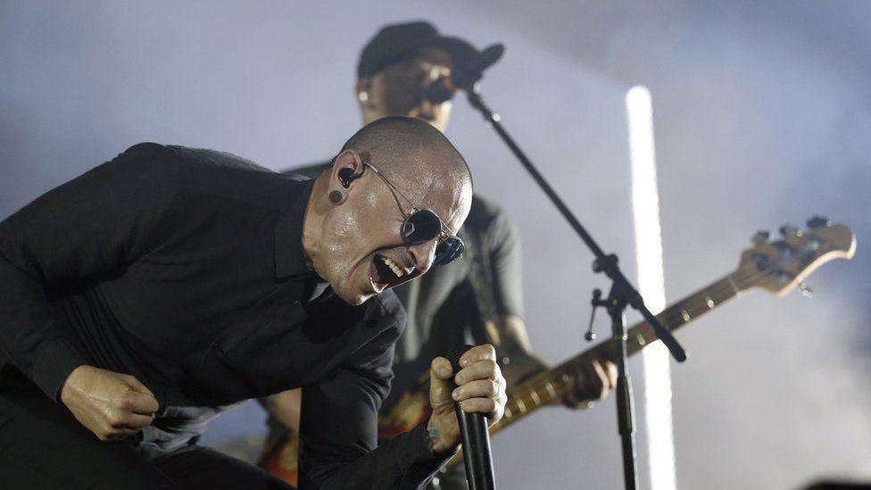 Linkin Park lead singer Chester Bennington screams into a microphone while performing at a live show.