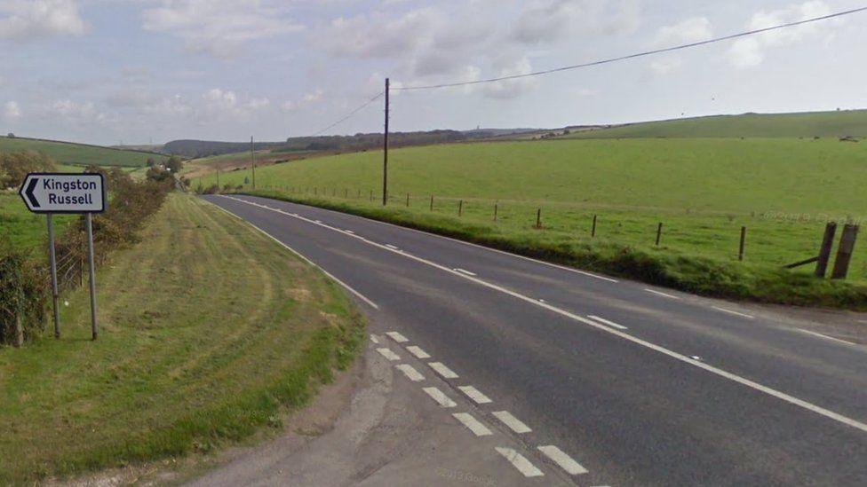 Green fields with side of a road and junction with black and white road sign on verge.