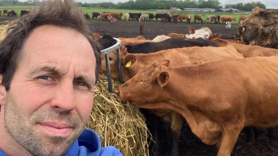 Lee Smith looking at camera with cattle behind him