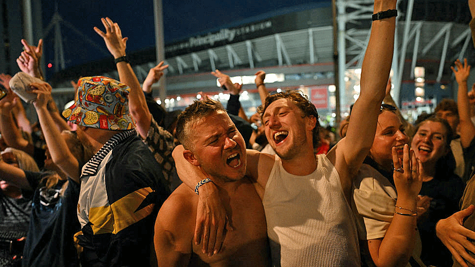 Fans hug and sing outside the stadium after the concert