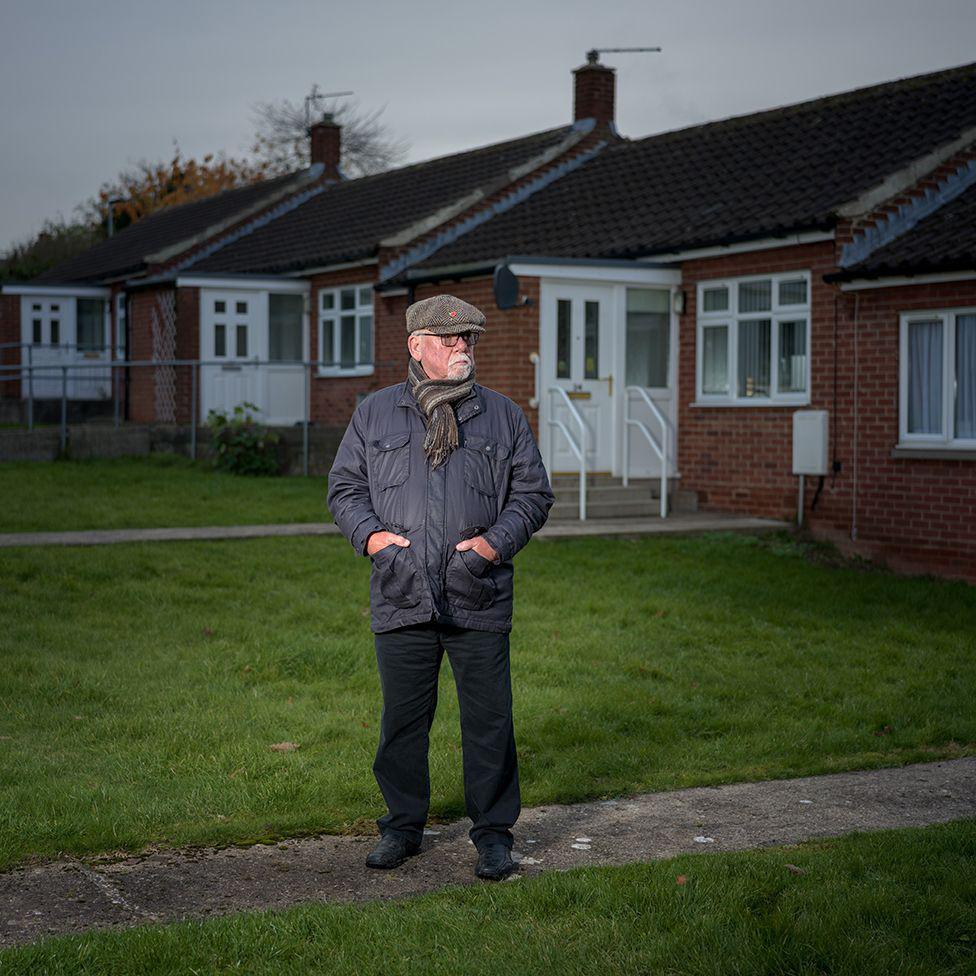 Former miner Walter Sherriff standing in front of a row of houses