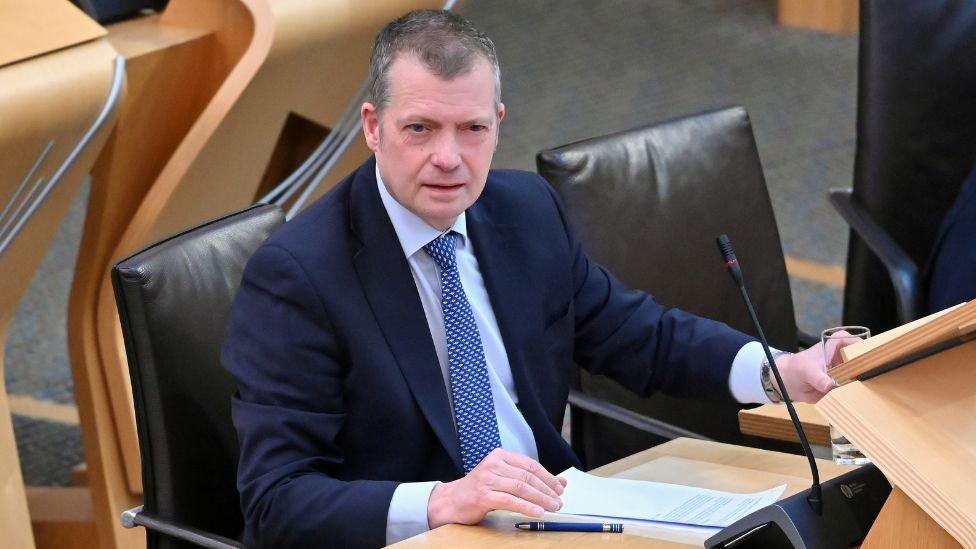 Graham Simpson, with grey hair and wearing a dark blue suit and lighter blue tie, sits in the Scottish Parliament chamber 