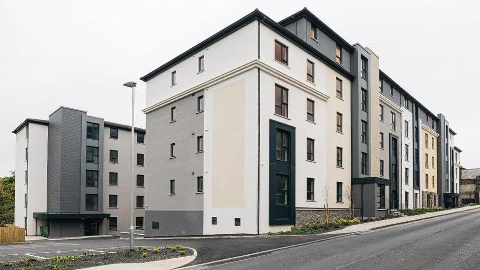 The exterior of two modern blocks of flats, which are coloured white, grey and beige on Peel Road.