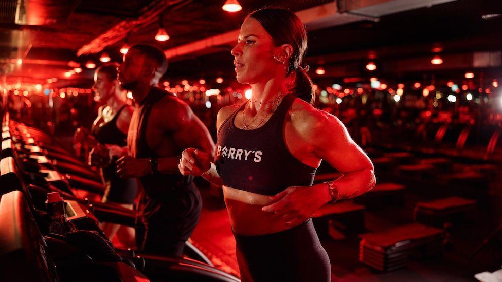 Tana running on a treadmill in a sports bra, illuminated by red light.