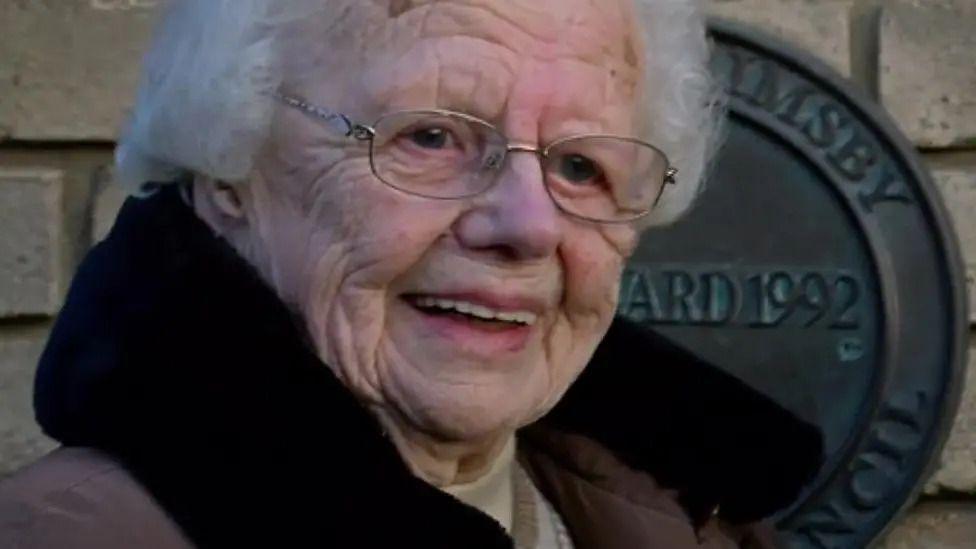 Brenda Fisher. She is standing in front of a plaque. 