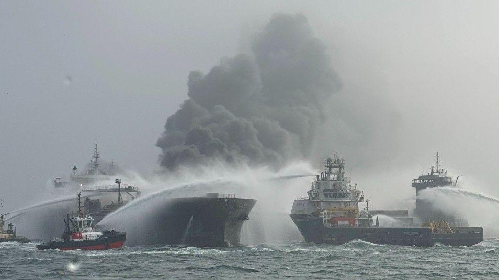 The Solong and Stena Immaculate ships. Water is being used to extinguish the fire and a large plume of grey smoke is above the ships.