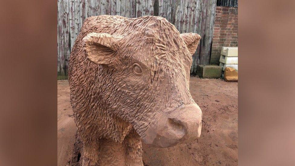 Close-up photo of a sculptured reddish brown cow. It has several lines on it to depict its coat, a large nose pointed to the side.