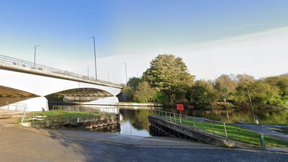 Road with double yellow lines and slipway with river behind and road bridge over the water