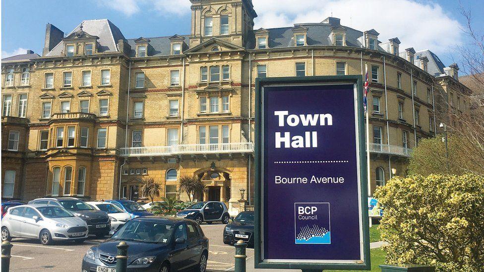 A large sign in front of a large sand-coloured building reads: "Town hall, Bourne Avenue". A car park is in front of the building.