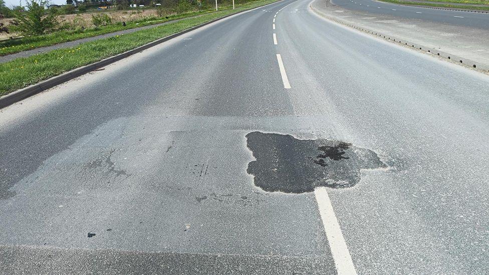 A view of a dual carriageway road with a large, dark piece of patching in the centre line