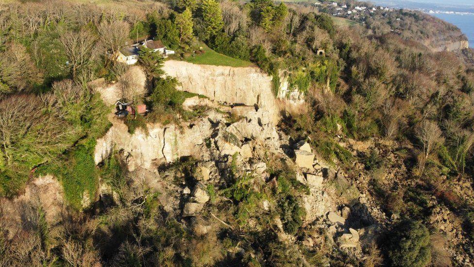 Buildings on the edge of the cliffs with chunks of cliffs, fallen trees and large cracks 