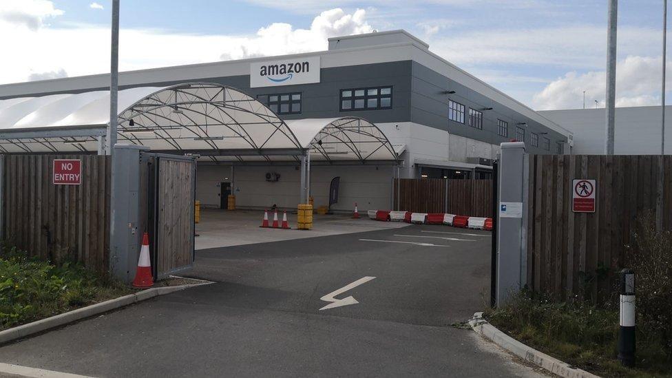A grey building in the distance with the 'amazon' sign. The gates to the compound is open.