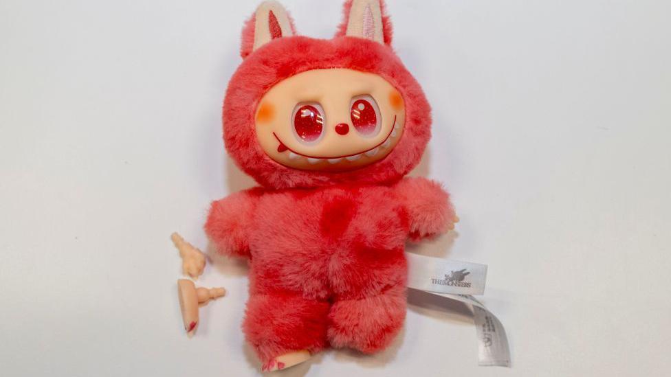 Fake Labubu toy, bright/pink colour, with bits fallen off.