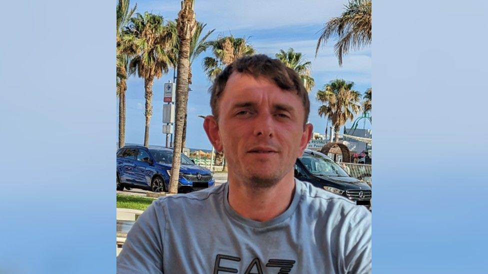 Andrew Peart in blue t-shirt, with cars and palm trees in the background.