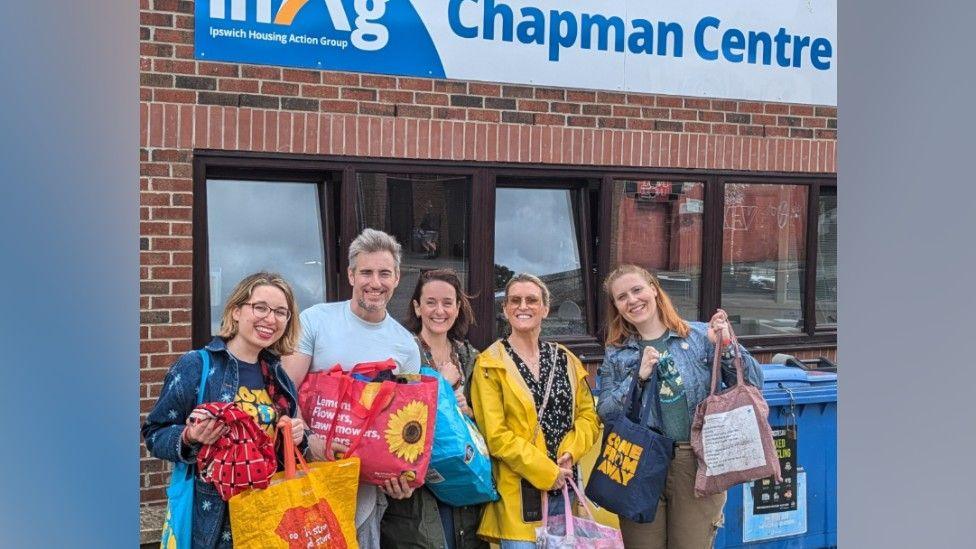 A group of five people holding shopping bags in front of the Ipswich Housing Action Group Chapman Centre. The picture includes four women and one man all looking and smiling at the camera.