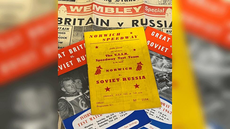 Old newspapers and speedway programmes from 1964, including a headline that says Wembley special Britain v Russia, and the Norwich Speedway programme, on bright yellow paper with red lettering. It states the USSR Speedway Test Team Norwich v Soviet Russia Friday, July 10th at 7.45pm 