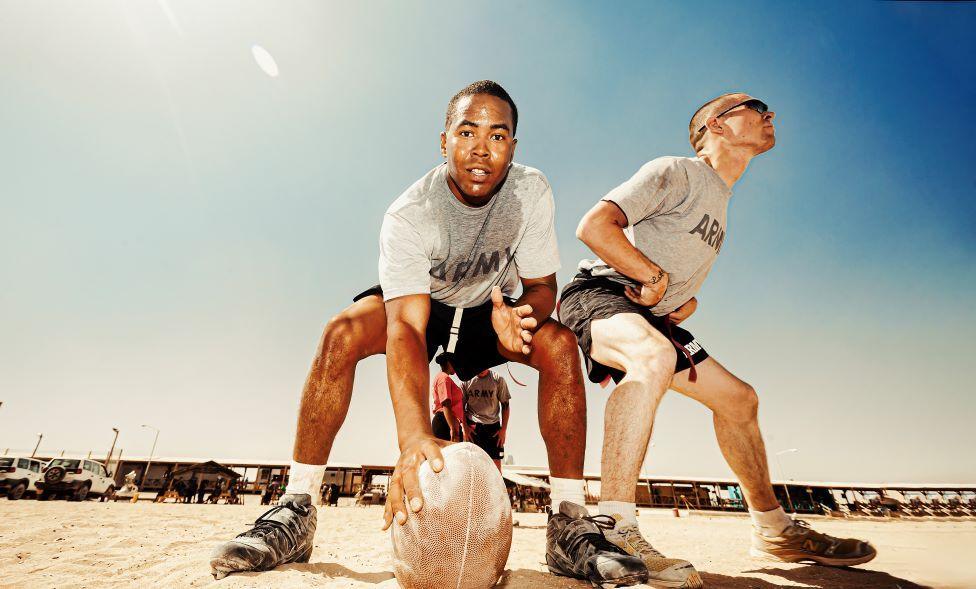 Two soldiers playing American Football in Afghanistan. They are wearing US Army T-shirts and shorts.