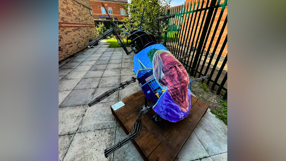 Side view of a large tansy beetle sculpture with a colourful portrait of Rosie Wall painted on its back