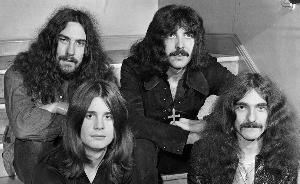 The four members of Black Sabbath sitting on stairs in a corridor in 1970