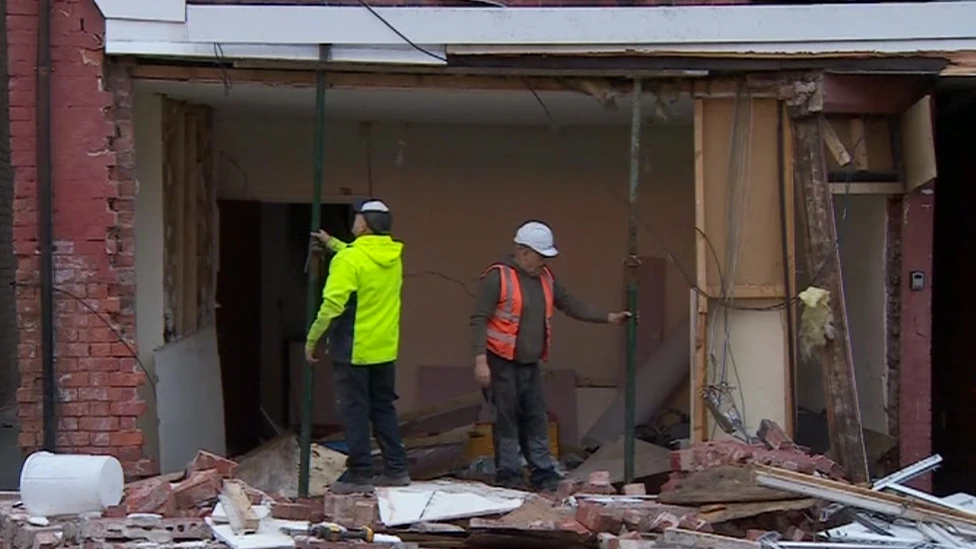 Two men in protective gear putting in poles to shore up the second storey of a building following an explosion
