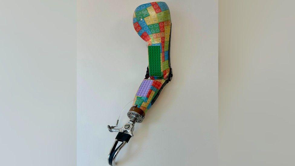 The prosthetic arm. It's painted with multicoloured Lego bricks, but there are also two pieces of actual Lego - one green and one purple - attacked to the front.