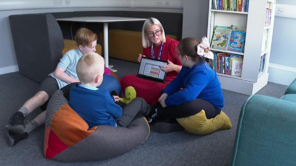 School pupils sat with headteacher Nicola Adams on the floor in a room at their school 