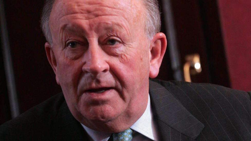 Stewart Spence, man wearing a dark striped suit, white shirt, and patterned tie.