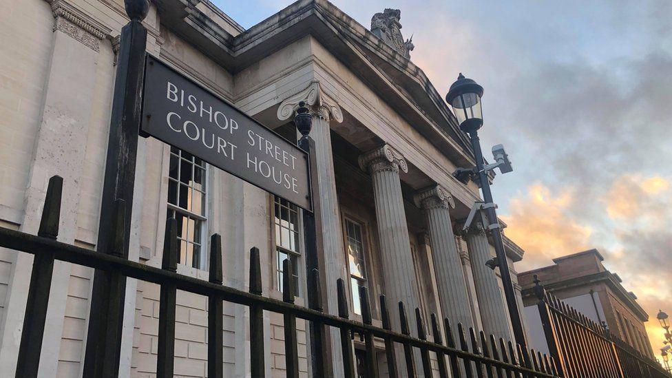 The front of Londonderry Court house,  including four big concrete pillars, as seen through the railings on the outside of the building.