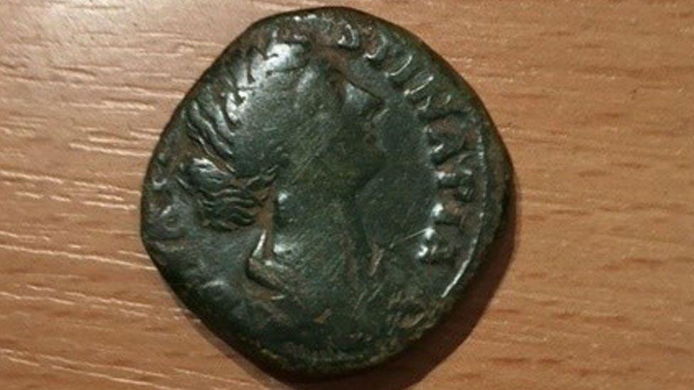 A Roman coin showing the head of a woman in profile, with a bun, and with letters on its edge