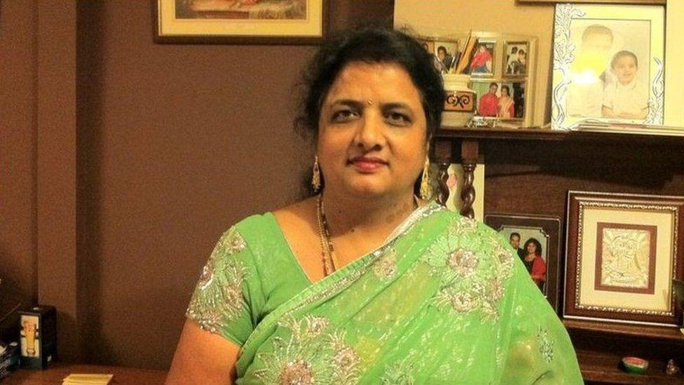 Neelam Aggarwal-Singh with long dark hair wearing a green saree and sitting in front of shelves holding family photographs